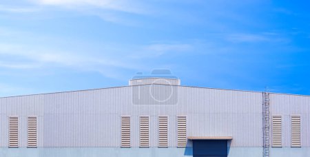 Foto de Gran pared de aluminio con ventilación de persiana y escalera de cilindro del edificio industrial de fábrica contra el fondo azul del cielo en vista panorámica, vista frontal con espacio para copias - Imagen libre de derechos