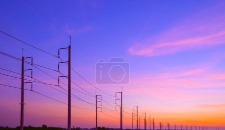 Silhouette two rows of electric poles with cable lines on curve country road against colorful sunset sky background after sundown, perspective side view