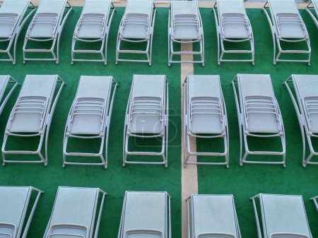 Téléchargez les photos : Chaises longues pliées grises alignées en rangées sur un pont de couleur verte à bord d'un paquebot de croisière sans bains de soleil. - en image libre de droit