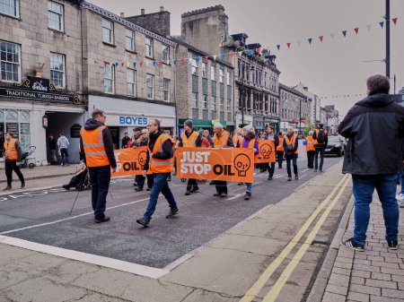 Téléchargez les photos : Les manifestants du groupe de pression Just Stop Oil marchent très lentement sur la route ralentissant la circulation pour protester contre les licences gouvernementales de forage pour le pétrole à Kendal, Cumbria, Royaume-Uni. - en image libre de droit