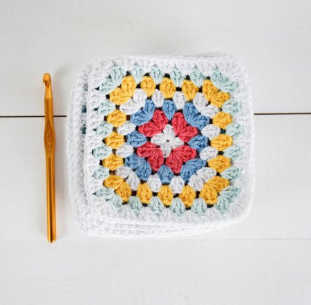 multicolored granny squares with crochet hook and white wooden ground handmade