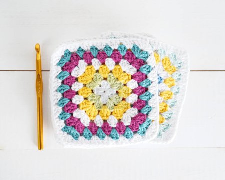 multicolored granny squares with crochet hook and white wooden ground handmade