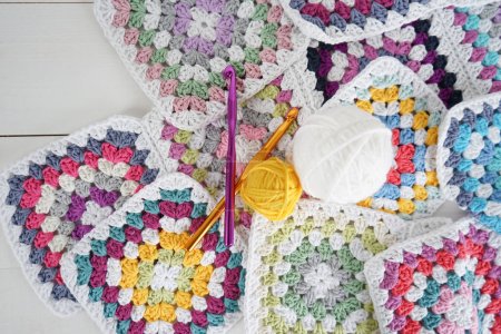 Téléchargez les photos : Boules de laine colorées avec carrés granny multicolores et crochets sur fond blanc en bois fait main - en image libre de droit
