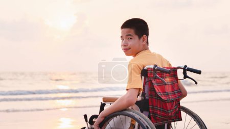 Foto de Niño asiático con cara feliz en la playa del mar puesta del sol, Hermoso momento de la naturaleza, Viajar con una silla de ruedas para aprender sobre el mundo sin límites con el apoyo de la familia, Buena salud mental, foto positiva - Imagen libre de derechos