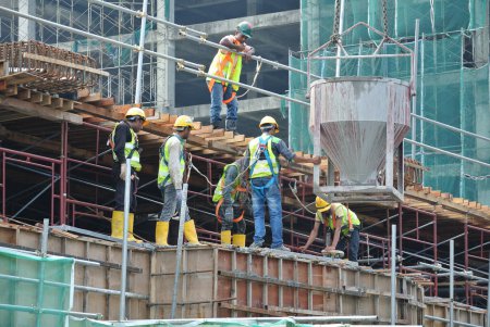 Téléchargez les photos : JOHOR, MALAISIE - 12 MAI 2016 : Un groupe de travailleurs de la construction versant du béton à l'aide d'un godet en béton dans le coffrage de la colonne sur le chantier de construction. - en image libre de droit