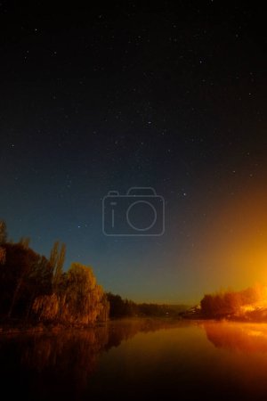 Photo for Starry sky over a large body of water with willows on the shore with a beautiful warm light. High quality photo - Royalty Free Image