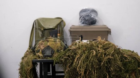Foto de A snipers helmet and camouflage suit are lying on a table with other military equipment. High quality photo - Imagen libre de derechos