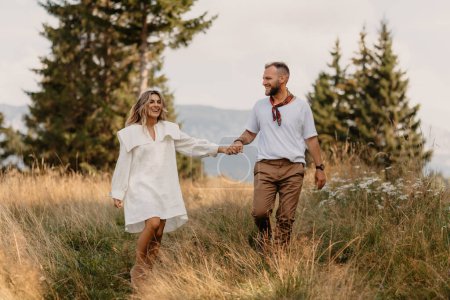 Outdoor-Aufnahme eines verliebten jungen Paares beim Spazierengehen durch eine Wiese im Gebirge