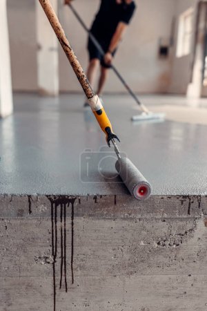 Foto de Un trabajador de la construcción aplica resina epoxi gris en una sala industrial - Imagen libre de derechos
