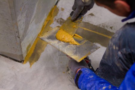 The professional is skillfully filling the expansion joints with epoxy mortar using a trowel and putty knife, ensuring that the material is spread evenly and completely fills the joint