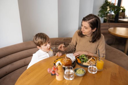Photo for A young and stylish mother and her adorable blond son bond over a healthy brunch at a trendy cafe, savoring nutritious and delicious dishes. This heartwarming moment captures the concept of healthy eating in the city - Royalty Free Image