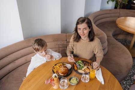 Photo for A young and stylish mother and her adorable blond son bond over a healthy brunch at a trendy cafe, savoring nutritious and delicious dishes. This heartwarming moment captures the concept of healthy eating in the city - Royalty Free Image