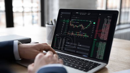 Market growth, profit, trading. Businessman, trader sits at workplace desk with laptop, makes analysis of long-term investments, check stock, cryptocurrency statistics data shown in graphs and charts