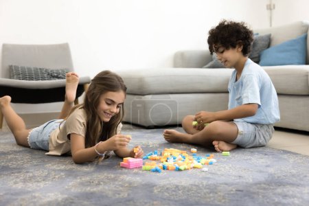 Téléchargez les photos : Deux enfants heureux mignons frères et sœurs empilant des blocs de construction de jouets sur le sol chaud de moquette, jouant au jeu créatif d'apprentissage à la maison, appréciant l'amitié, l'enfance, l'activité intelligente, le temps de jeu - en image libre de droit