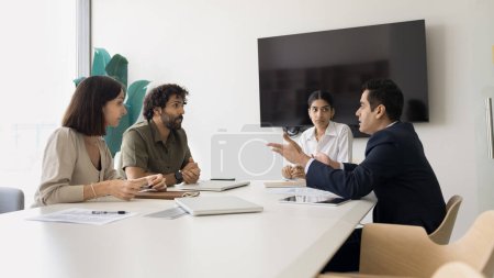 Photo for Serious diverse business colleagues discussing work on project, management strategy, meeting at table in boardroom. Young Indian leader woman holding negotiation of partners - Royalty Free Image