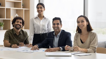 Foto de Retrato de oficina de equipo de negocios multiétnicos con éxito positivo. India feliz, árabe, colegas latinos sentados en la mesa de reunión juntos, mirando a la cámara, sonriendo, riendo - Imagen libre de derechos