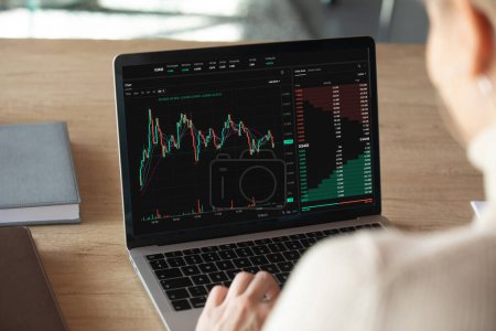 Close up laptop screen view with stocks charts and graphs over shoulder of female crypto trader, analyze financial stock, makes trade market research, buy or sell cryptocurrency, review risk or profit