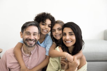 Téléchargez les photos : Des parents latins joyeux qui soutiennent des enfants préadolescents, posant pour un portrait de famille à la maison, regardant la caméra avec des sourires de dents, riant, appréciant la garde d'enfants, la parentalité - en image libre de droit