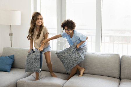 Photo for Happy excited preteen sibling kids fighting with pillows on big soft couch, playing active games at home, having fun, laughing, enjoying family leisure, playtime, childhood, friendship - Royalty Free Image