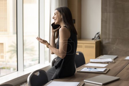 Photo for Cheerful Hispanic manager woman speaking on cellphone in office boardroom, enjoying phone talk to client, making call, laughing, using gadget for wireless connection in office - Royalty Free Image
