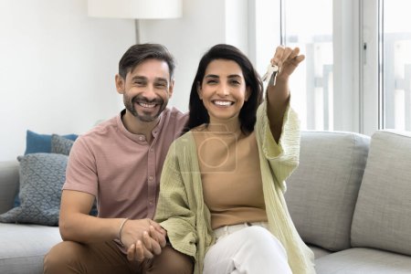 Photo for Happy excited middle aged couple showing keys after moving into new house, sitting on comfortable couch, hugging, looking at camera, smiling, laughing, posing family for portrait - Royalty Free Image