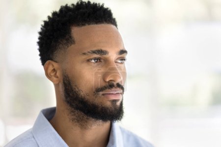 Photo for Serious handsome young African man indoor casual portrait. Thoughtful dreamy barber model, Black guy with stylish beard posing indoors, looking away in deep thoughts. Close up shot - Royalty Free Image