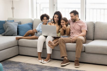 Photo for Cheerful sweet preteen kids and couple of parents enjoying leisure with laptop on spacious comfortable home couch, using smart technology, media service for watching movie - Royalty Free Image