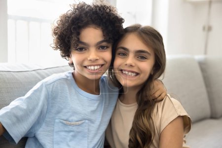 Happy Latin preteen brother and sister kids posing for family portrait at home, hugging, looking at camera with toothy smile, laughing, enjoying friendship, funny leisure, bonding