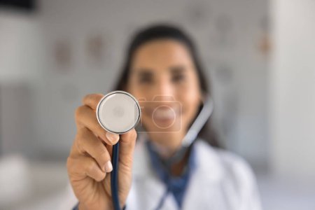 Photo for Hand of young doctor woman showing stethoscope at camera. Close up of medical tool, instrument for checking heartbeat rate, breathing kung, heart work with nurse, medical worker in blurred background - Royalty Free Image