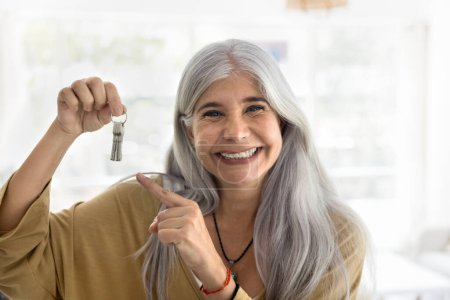 Téléchargez les photos : Heureuse femme latine âgée retraitée montrant les clés de la nouvelle maison, souriante, promouvant l'hypothèque, louant le service d'agence d'appartement, achat immobilier, regardant l'appareil photo, souriant, posant pour le portrait - en image libre de droit