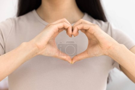 Photo for Young woman showing hand heart shape at camera, joining fingers at chest, expressing love, affection, romance, promoting kindness, friendship. Cropped close up shot of arms - Royalty Free Image