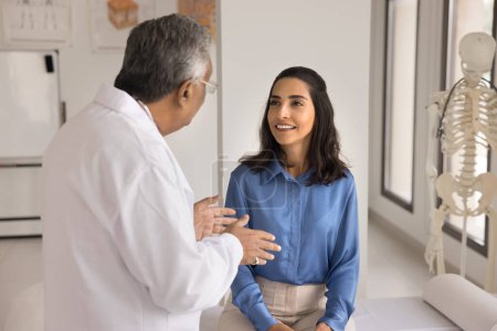 Photo for Happy young Hispanic patient woman consulting senior Indian doctor man, visiting practitioner in clinic office, listening to treatment advice after medical checkup, sitting on couch, smiling - Royalty Free Image