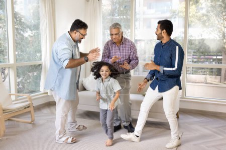 Téléchargez les photos : Heureux hommes indiens de trois générations familiales et petit enfant dansant à la maison ensemble, célébrant l'événement familial. Fille avoir du plaisir, profiter du mouvement, l'activité avec papa, grand-père et arrière grand-père - en image libre de droit