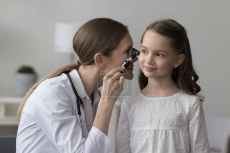 Laryngologiste féminine en manteau blanc à l'aide d'un otoscope professionnel examinant l'oreille de la petite fille lors de sa visite à la clinique. Otolaryngologie, santé des enfants, prévention des infections inflammatoires
