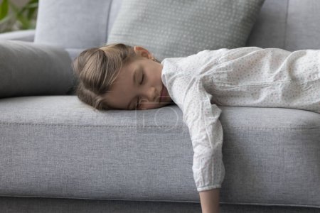 Photo for Tired little lazy girl lying down, sleeps on sofa in living room, resting, take break after difficult school day, relaxing, having healthy daytime nap, looks without energy, no motivation, close up - Royalty Free Image