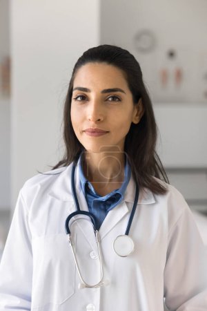 Photo for Positive beautiful young practitioner woman vertical portrait. Medical worker, doctor, therapist with stethoscope on neck looking at camera, posing in clinic office, promoting healthcare checkup - Royalty Free Image