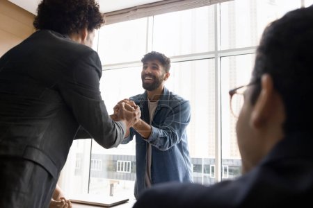 Photo for Positive excited project managers celebrating team success, holding stacked hands over meeting table with gratitude, laughing. Happy young Arab business professional thanking colleague for help - Royalty Free Image