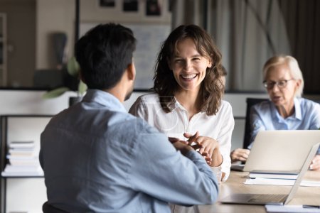 Photo for Cheerful young employee woman discussing project with colleague at meeting table, laughing, having fun, talking to coworkers. Two managers enjoying communication at office meeting - Royalty Free Image
