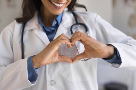 Photo for Cropped shot of young doctor woman showing hand heart, keeping romantic finger gesture at chest, expressing love, care, support for patients, early cardio disease diagnosing, checkup. Close up - Royalty Free Image