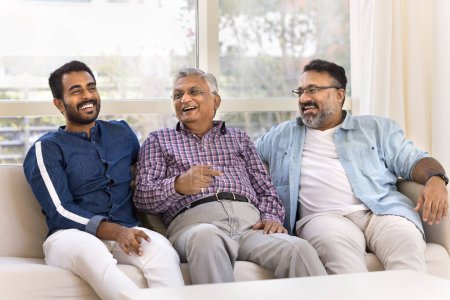 Photo for Cheerful elder Indian grandfather, father, young adult son and grandson talking on home couch, laughing, having fun, enjoying family relations, friendship, communication - Royalty Free Image