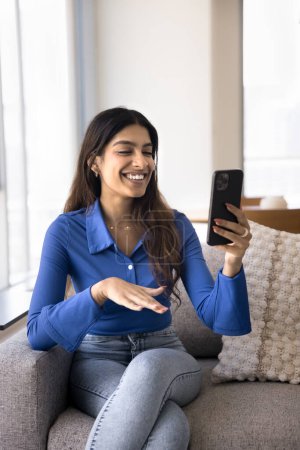 Foto de Joven joven alegre chica india hablando en el teléfono inteligente, charlando con un amigo, hablando en videollamada en línea, sonriendo, riéndose de la conversación, disfrutando de la comunicación por Internet. Disparo vertical - Imagen libre de derechos