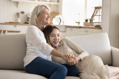 Photo for Middle aged happy woman spend time on cozy sofa with cute pre-teen daughter, enjoy tender moment, have friendly conversation, show love, care and good relationship. Two female generation relax at home - Royalty Free Image