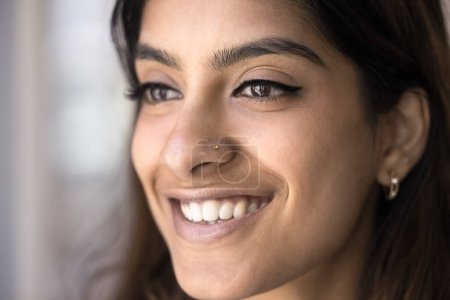 Téléchargez les photos : Joyeux beau visage jeune femme indienne de près. Fille modèle de soins de beauté positive avec une peau faciale parfaite lisse, patient dentaire avec sourire aux dents regardant loin, posant pour macro portrait - en image libre de droit