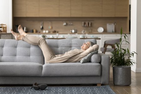 Foto de Mujer madura feliz pacífico tumbado en el sofá relajarse en la sala de estar, disfrutar de un fin de semana perezoso en casa, soñar, sonreír, respirar aire fresco, sentirse despreocupado, descansar después de la jornada laboral en el sofá cómodo. Pasatiempo - Imagen libre de derechos