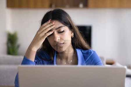 Photo for Exhausted overworked young Indian freelancer woman touching head with closed eyes at laptop, feeling headache, suffering from migraine, fatigue, burnout, thinking on work problems - Royalty Free Image