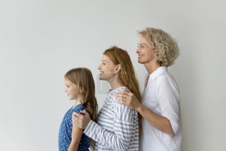 Photo for Little girl her young adult mummy and mature grandma posing on gray studio wall background, showing unity, deep-rooted connections, shared history among family members across different stages of life - Royalty Free Image