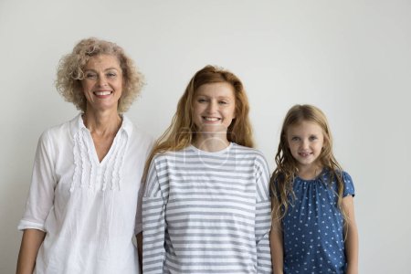 Téléchargez les photos : Trois belles femmes souriantes de parents posant sur fond de studio gris, regardant la caméra, se sentent heureuses, montrant des liens familiaux et l'unité. Hérédité, de l'enfance au milieu de la vie, cours de la vie, vie - en image libre de droit