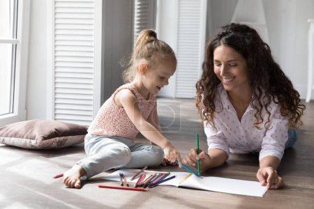 Photo for Caring babysitter drawing pictures with pencils spend time at home with little cute girl, settled down together on warm floor, enjoy creative hobby and communication. Family pastime, kid development - Royalty Free Image