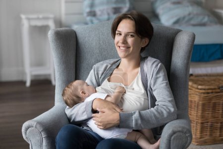 Photo for Portrait of loving mother sit on cozy armchair breastfeeding newborn in modern bedroom smile look at camera, enjoy sweet moments of tenderness and happy motherhood. Maternity, infancy, natural growth - Royalty Free Image