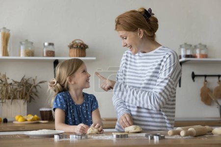 Photo for Little beautiful girl helper cooking with loving young mother, kneading dough, preparing sweet homemade cookies on holiday in cozy kitchen. Parent teach kid to cook, sharing traditional family recipe - Royalty Free Image
